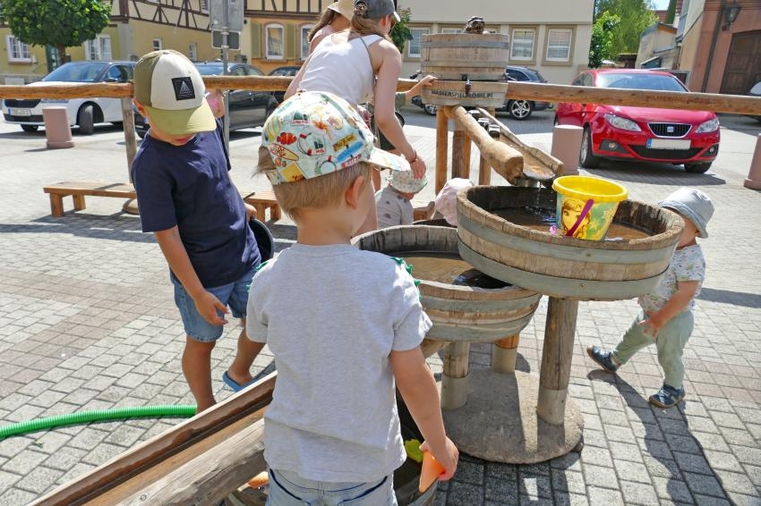 Kinder spielen am Wasserspeilmobil auf dem Marktplatz
