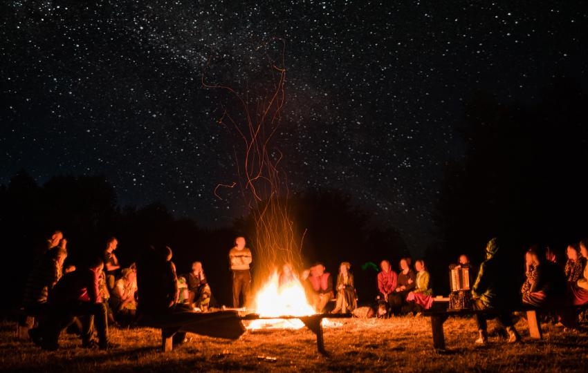 Menschen sitzen am Abend auf Bänken um ein Lagerfeuer © Adobe Stock